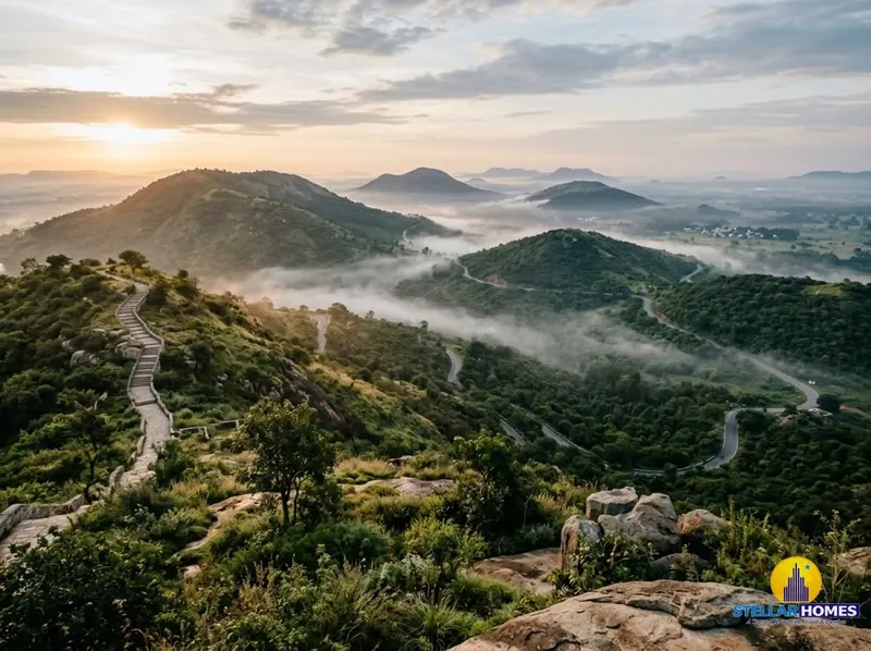 Golden sunrise over the misty green hills of Nandi Hills, with a stone stairway trail along the ridge and winding roads through the valley below