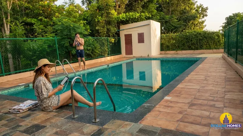 A resident reading by the pool steps in a sunhat while another resident dries off poolside, with green fencing and trees around the deck